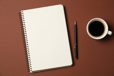 Photo of Notebook with pen and coffee on brown background, flat lay