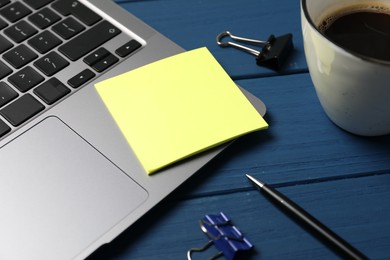 Photo of Laptop with sticky note, pen, paper clips and coffee on blue wooden table, closeup