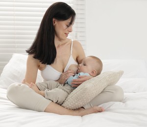 Photo of Smiling mother breastfeeding her little baby on bed at home