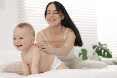 Photo of Smiling mother with her little baby on bed at home, selective focus
