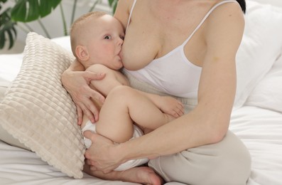 Photo of Mother breastfeeding her little baby on bed indoors, closeup