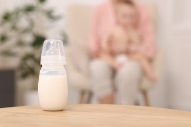 Photo of Mother with her little baby indoors, focus on bottle of milk