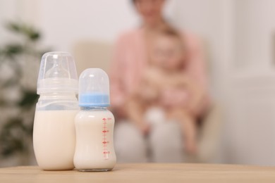 Photo of Mother with her little baby indoors, focus on bottles of milk