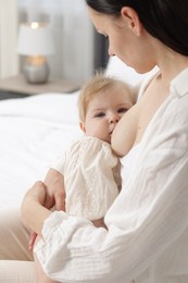 Photo of Mother breastfeeding her little baby on bed indoors