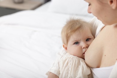 Photo of Mother breastfeeding her little baby on bed indoors, closeup. Space for text