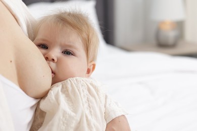 Photo of Mother breastfeeding her little baby on bed indoors, closeup. Space for text