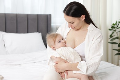 Photo of Mother breastfeeding her little baby on bed indoors