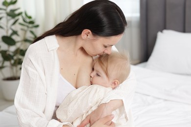 Photo of Mother breastfeeding her little baby on bed indoors. Space for text