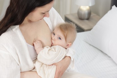 Photo of Mother breastfeeding her little baby on bed indoors