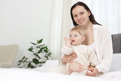 Photo of Smiling mother with her little baby on bed at home. Space for text