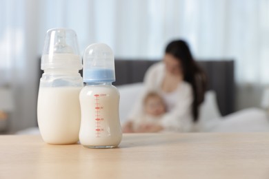 Photo of Mother with her little baby indoors, focus on bottles of milk