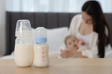 Photo of Mother with her little baby indoors, focus on bottles of milk