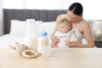 Photo of Mother with her little baby indoors, focus on bottles of milk and teether