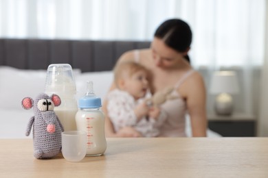 Photo of Mother with her little baby indoors, focus on bottles of milk and toy