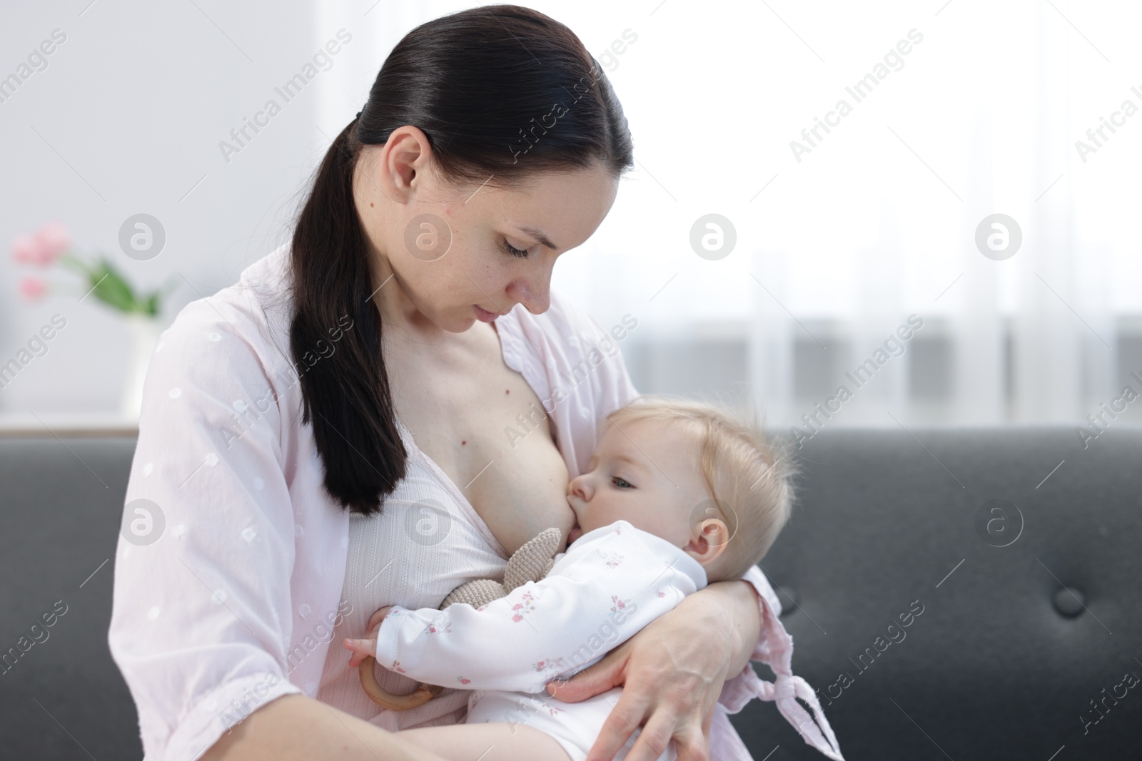 Mother breastfeeding her little baby on sofa indoors Photo of Mother breastfeeding her little baby on sofa indoors