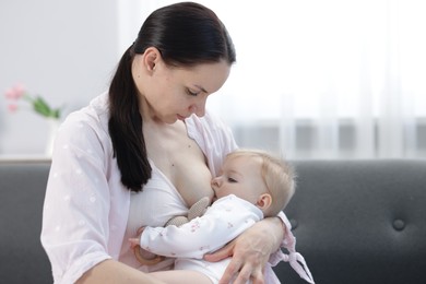 Photo of Mother breastfeeding her little baby on sofa indoors