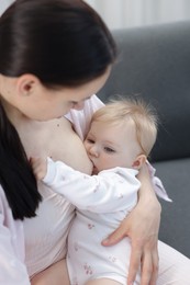 Photo of Mother breastfeeding her little baby on sofa indoors