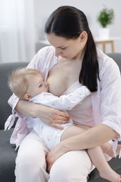 Photo of Mother breastfeeding her little baby on sofa indoors
