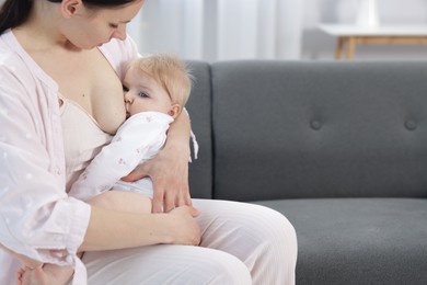 Photo of Mother breastfeeding her little baby on sofa indoors, closeup. Space for text