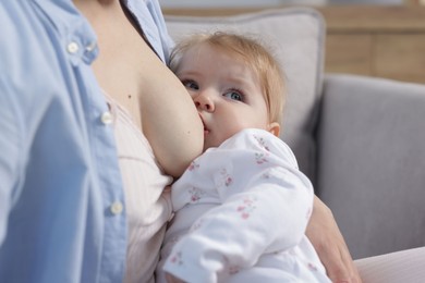 Photo of Mother breastfeeding her little baby on sofa indoors, closeup