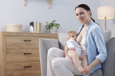 Photo of Smiling mother breastfeeding her little baby on armchair indoors. Space for text