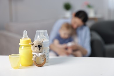 Photo of Mother with her little baby indoors, focus on bottles of milk and teether
