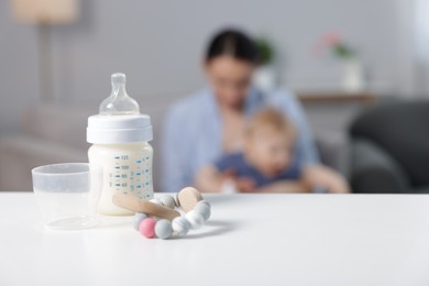 Photo of Mother with her little baby indoors, focus on bottle of milk and teether