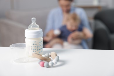 Photo of Mother with her little baby indoors, focus on bottle of milk and teether