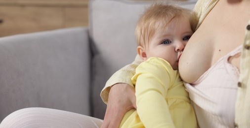 Photo of Mother breastfeeding her little baby on sofa indoors, closeup