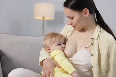 Photo of Mother breastfeeding her little baby on armchair indoors