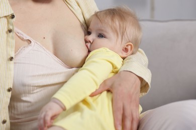 Photo of Mother breastfeeding her little baby on sofa indoors, closeup