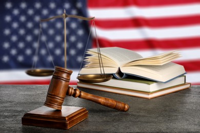 Image of Judge's gavel, scales of justice and books on grey table against flag of USA