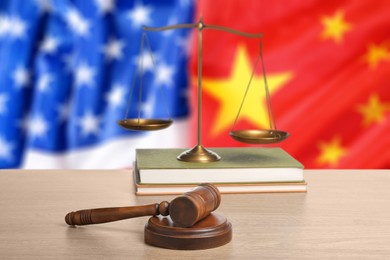 Image of Judge's gavel, scales of justice and books on wooden table against flags of USA and China