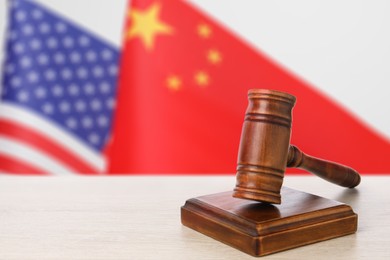 Image of Judge's gavel on wooden table against flags of USA and China