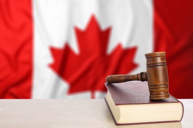 Image of Judge's gavel and book on table against flag of Canada
