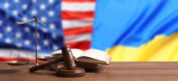 Image of Judge's gavel, scales of justice and books on wooden table against flags of USA and Ukraine. Banner design