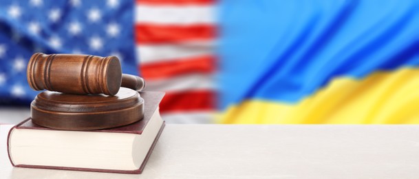 Image of Judge's gavel and book on white table against flags of USA and Ukraine. Banner design