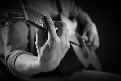 Image of Man playing guitar in darkness, closeup. Black and white effect