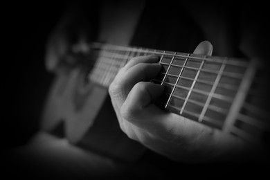 Image of Man playing guitar in darkness, closeup. Black and white effect
