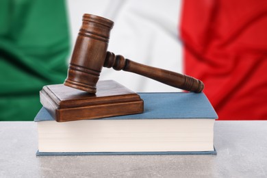 Image of Judge's gavel and book on grey table against flag of Italy