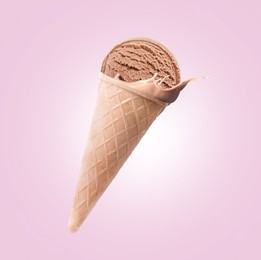 Image of Chocolate ice cream in waffle cone and splash of milk in air on pink background