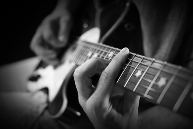 Image of Man playing guitar in darkness, closeup. Black and white effect