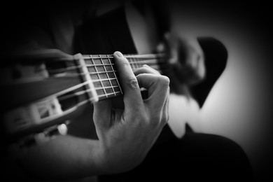 Image of Man playing guitar on dark background, closeup. Black and white effect