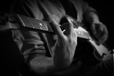 Image of Man playing guitar in darkness, closeup. Black and white effect