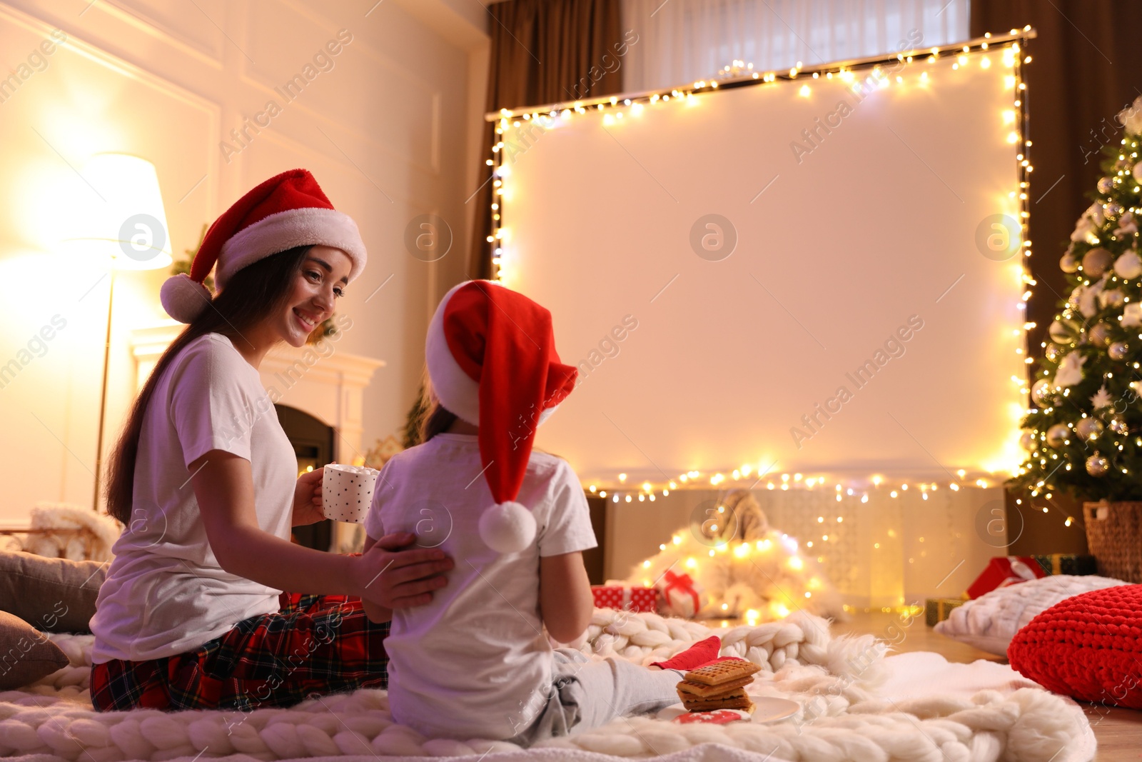 Mother and daughter watching movie using video projector at home. Cozy Christmas atmosphere Photo of Mother and daughter watching movie using video projector at home. Cozy Christmas atmosphere