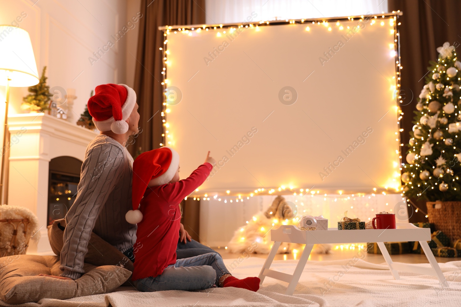 Photo of Father and daughter watching movie using video projector at home. Cozy Christmas atmosphere