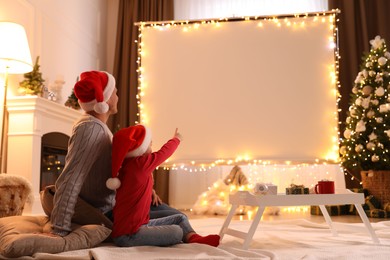 Photo of Father and daughter watching movie using video projector at home. Cozy Christmas atmosphere
