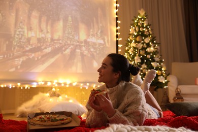 Photo of MYKOLAIV, UKRAINE - DECEMBER 24, 2020: Woman watching Harry Potter and Philosopher's Stone movie via video projector in room. Cozy winter holidays atmosphere