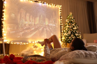 Photo of MYKOLAIV, UKRAINE - DECEMBER 24, 2020: Woman watching Harry Potter and Philosopher's Stone movie via video projector in room. Cozy winter holidays atmosphere