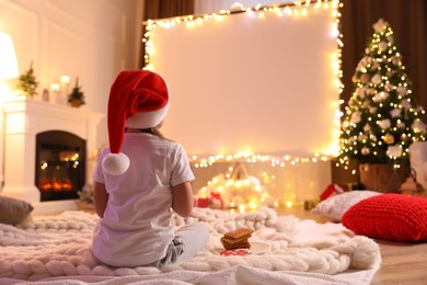 Photo of Little girl watching movie using video projector at home. Cozy Christmas atmosphere